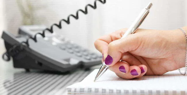 Une main prend des notes à côté d'un téléphone de bureau